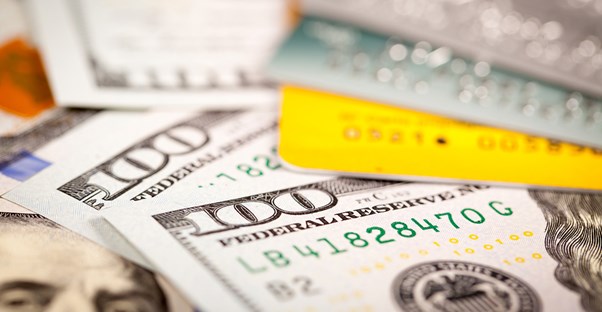 Credit cards and one hundred dollar bills piled up to represent how credit card consolidation can cost you.