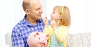 Man uses a piggy bank to explain saving money and budgeting to his young daughter.