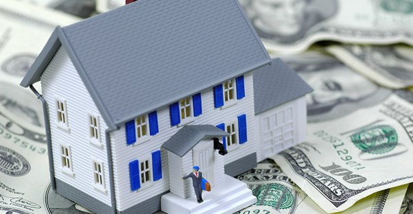 A plastic toy house sitting on a pile of money to represent how you qualify for a home loan.
