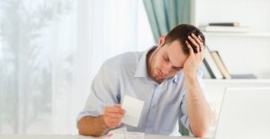 Man rests his head in his hand as he tries to decide which debt he needs to pay off first.