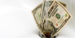 A ten dollar and two one dollar bills being washed down the drain to represent that impulse purchases are a waste of money.