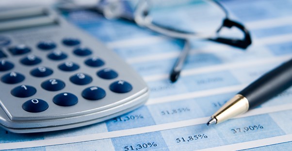 A pen and calculator sitting on top of financial documents as someone calculates their Social Security benefits.