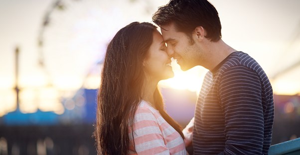 a couple embraces in front of a sunset and ferris wheel