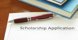 After researching financial aid options, a future college student leaves a scholarship application sitting on a desk with a pen and stack of books.