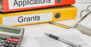 Folders for grants and applications piled on a desk next to other documents need to qualify for the Pell Grant and it's advantages.