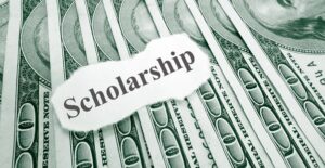 A piece of paper saying SCHOLARSHIP laying on top of money earned by finding available college scholarships.