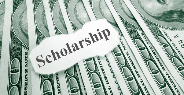 A piece of paper saying SCHOLARSHIP laying on top of money earned by finding available college scholarships.