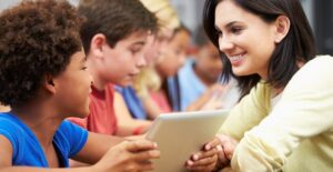 students use tablets while a teacher looks on