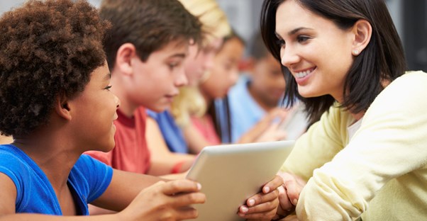 students use tablets while a teacher looks on