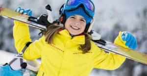 a young girl energetically carries her skis through the snow