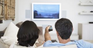 A couple watches TV while discussing if they should buy an extended warranty.