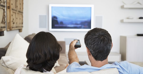 A couple watches TV while discussing if they should buy an extended warranty.
