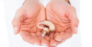 Two hands gently cup a hearing aid