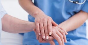 CNA holds the hand of a patient to soften the blow of the bad news she's about to give