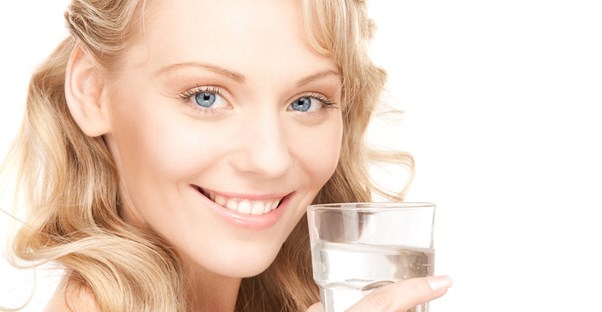 Young woman smiles as she drinks water and improves her skin health.
