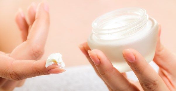 A woman scoops moisturizer out of a jar to apply to her oily skin.