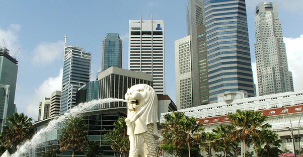 a singapore merlion fountain sprays water in front of the singapore skyline