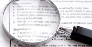 A magnifying glass lies on top of a list of requirements