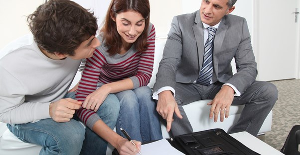 A young couple sign papers to purchase their first home with a real estate agent