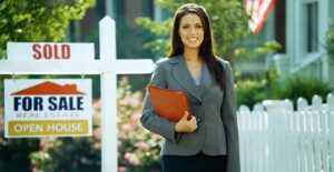 Real estate agent smiles and stands in front of a sold sign