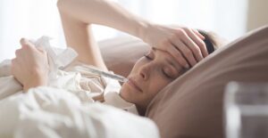 Sick woman lies in bed with thermometer in her mouth