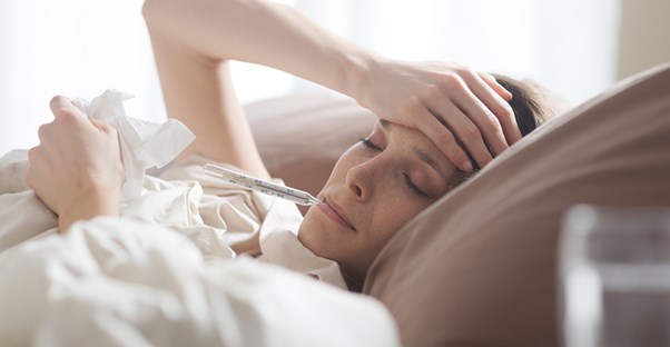 Sick woman lies in bed with thermometer in her mouth