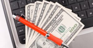 Money on a laptop with a pen across it