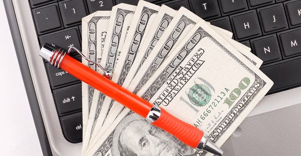 Money on a laptop with a pen across it
