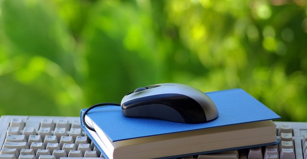 A mouse sits upon a book which sits upon a keyboard