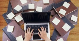 A laptop is surrounded by books and sticky notes