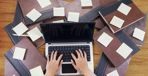 A laptop is surrounded by books and sticky notes