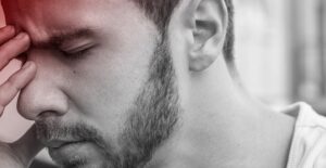 A man grasps his forehead in pain as a migraine headache occurs.