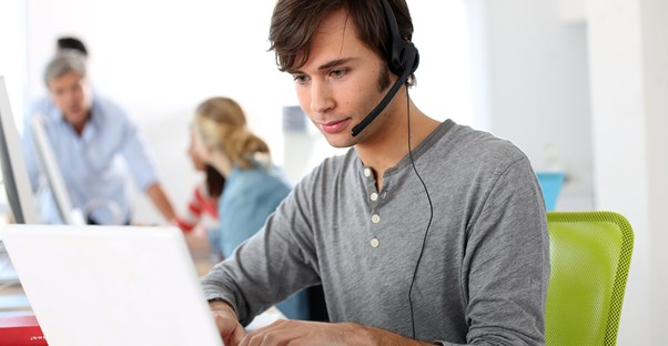 Man types on his laptop and speaks into his bluetooth headset