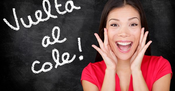 Girl flashes a huge smile while standing in front of a chalkboard with spanish written on it