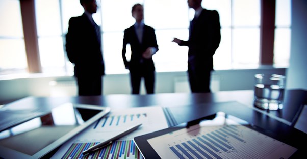 Men in suits talking in behind of a table stacked with graphs