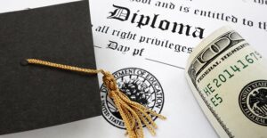 Graduation cap and hundred dollar bill sitting on a diploma