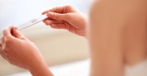 A woman checks a pregnancy test that shows two red lines.