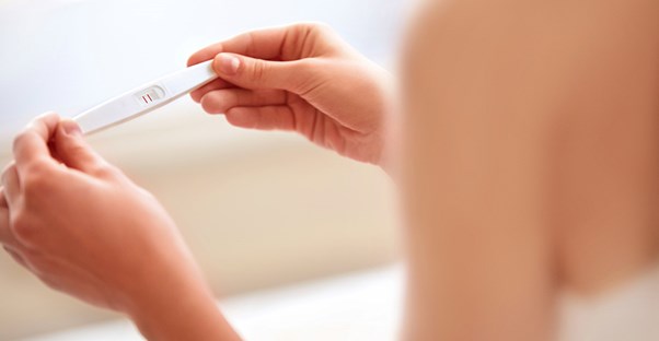 A woman checks a pregnancy test that shows two red lines.