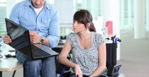 Man sitting on table showing laptop to woman in wheelchair
