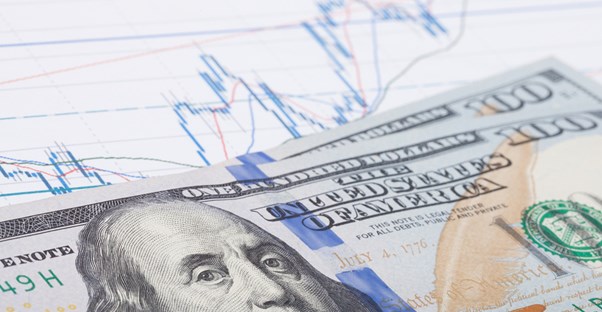 100 dollar bills laying on a print out of the stock market