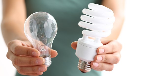 Woman holding out an energy efficient light bulb next to a regular light bulb.