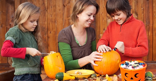 A mom helping her kids carve jack-o-lanterns