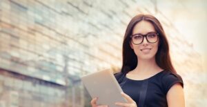 Girl with brown hair and glasses holds up a tablet