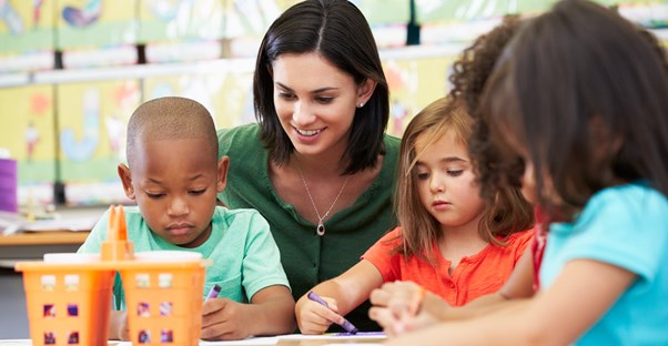 A teacher watches her students draw and color