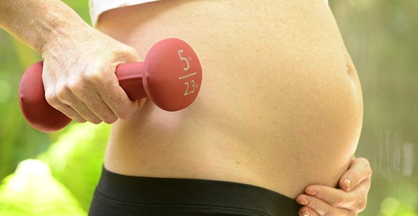 A pregnant woman holds a 5 pound weight.