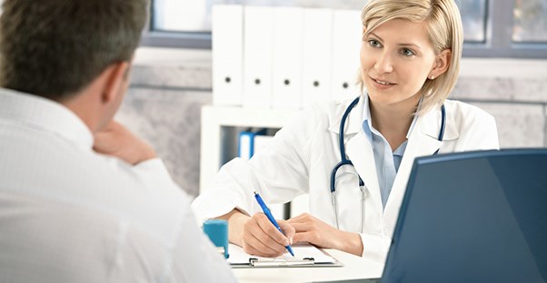 A doctor takes notes in her office while she is talking to a patient.