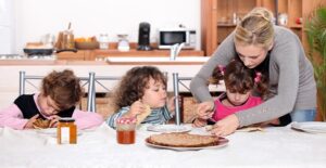 A nanny helps a little girl cut up her food
