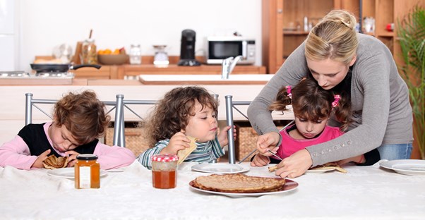 A nanny helps a little girl cut up her food