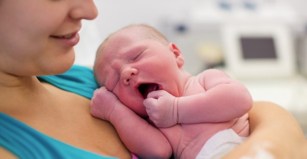 A woman holds her newborn baby on her chest as she lies in a hospital bed.