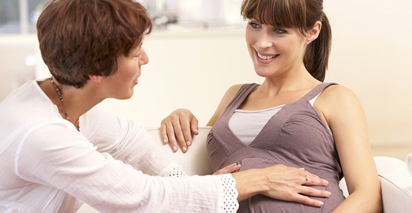 A doula speaks with a pregnant woman sitting on a couch.